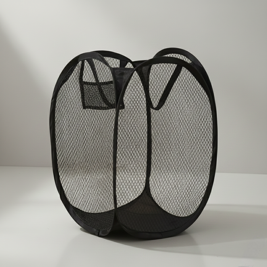Cesto de ropa sucia negro de malla transpirable, organizador plegable pop-up con asas y bolsillo sobre fondo neutro.
